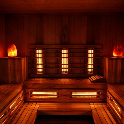 Wnętrze sauny infrared - podłogi i ściany pokryte drewnem, wzdłuż trzech ścian zamontowana jest drewniana ława, w rogach drewniane podesty z lampami w kształcie kryształów. Na ścianach i pod ławą widać pomarańczowe promienniki podczerwone. 