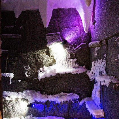 Wnętrze groty śnieżnej - ciemne kamienie na ścianach, warstwa śniegu na podłodze, wiszące stalaktyty z sufitu pokryte są śniegiem. Resztki śniegu znajdują się również na ścianach. Oświetlenie w kolorze fioletowym i niebieskim. 