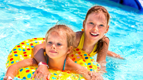 Dwie uśmiechnięte rudowłose dziewczynki pozują w basenie. Dziecko na pierwszym planie jest w dmuchanym kole do pływania.