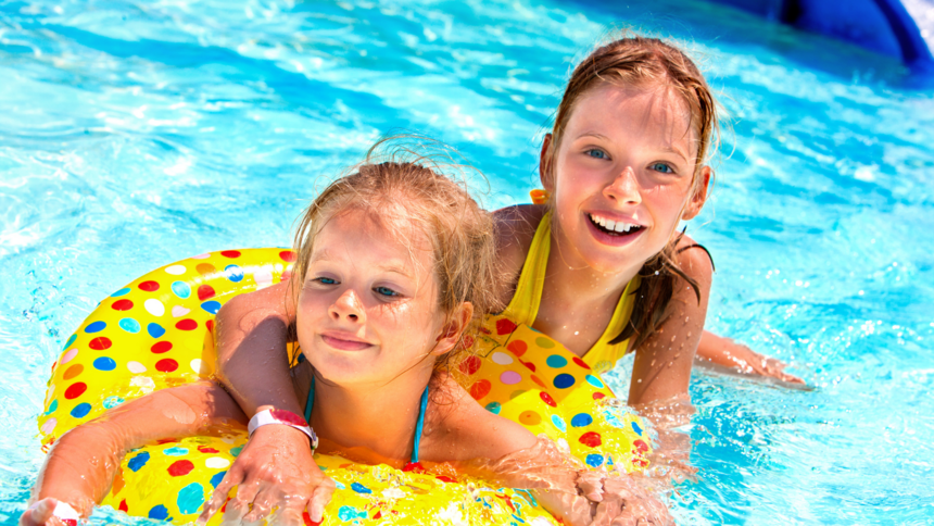 Dwie uśmiechnięte rudowłose dziewczynki pozują w basenie. Dziecko na pierwszym planie jest w dmuchanym kole do pływania.