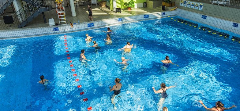 Wewnętrzny basen z falą. Na głębszej części grupa Falowiczów powtarza ćwiczenia prezentowane przez instruktora na brzegu.
