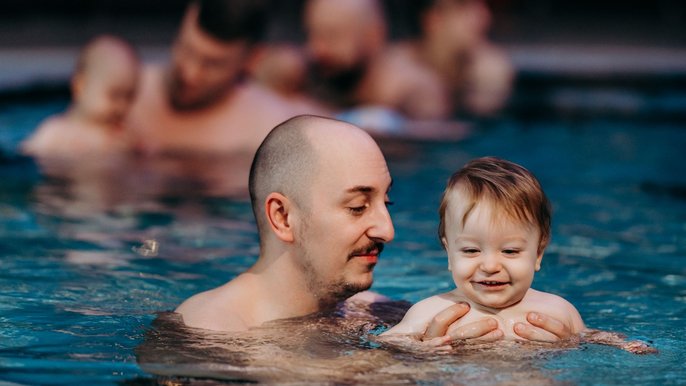 Mężczyzna trzymający uśmiechnięte dziecko w wodzie. 