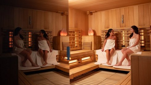 2 kobiety w ręcznikach siedzące na drewnianych ławach sauny fińskiej. 
