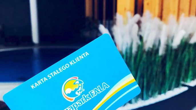 Na pierwszym planie niebieska karta z logotypem Aquaparku FALA z napisem Karta Stałego Klienta. W tle basen wody gorącej w Strefie Saun. 