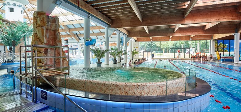 Basen solankowy w łezce pomiędzy wewnętrznym basenem sportowym a rekreacyjnym. Basen otoczony beżową mozaiką, obok niego brązowy wodospad z mgiełką solankową.