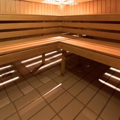 Wnętrze sauny fińskiej obite jasnym drewnem. Wzdłuż ścian drewniane ławy z dwoma rzędami siedzisk. 