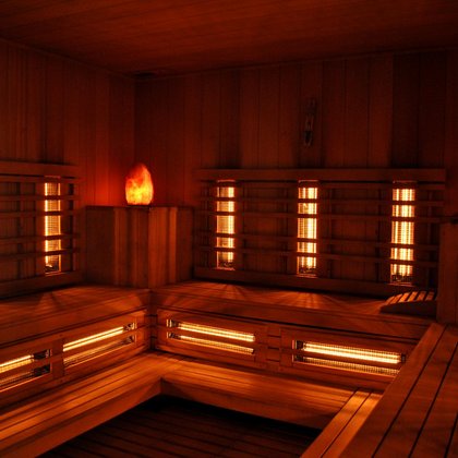Wnętrze sauny infrared - podłogi i ściany pokryte drewnem, wzdłuż trzech ścian zamontowana jest drewniana ława, w rogach drewniane podesty z lampami w kształcie kryształów. Na ścianach i pod ławą widać pomarańczowe promienniki podczerwone. 