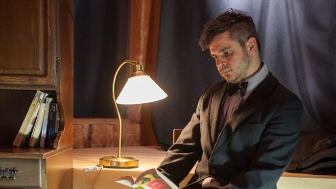 Saunamistrz Marcin Rogoziński - młody mężczyzna w garniturze z książką w ręku w ciepłym świetle lampy biurkowej. 