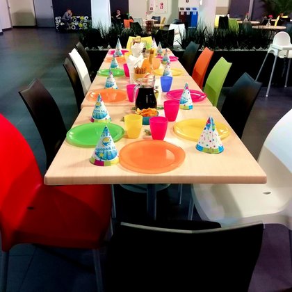 Urodzinowy stół zastawiony kolorową zastawą, przekąskami i kolorowymi czapeczkami urodzinowymi z logotypem Aquaparku FALA. 