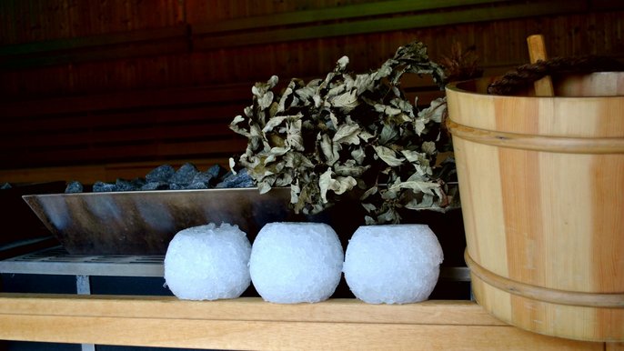 Zbliżenie na trzy kule lodowe, wiaderko do wody i witki brzozowe rozłożone na drewnianej obudowie pieca saunowego. 