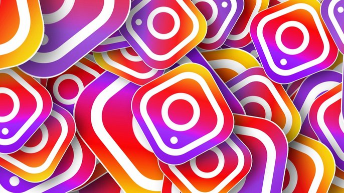 Kilkadziesiąt czerwono-żółto-fioletowych ikonek aplikacji Instagram nachodzących na siebie i wypełniających przestrzeń grafiki. Każda ikona to biały obrys imitujący kwadratowy aparat z okrągłym obiektywem. 