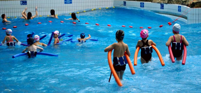 Basen z efektem fali - falowanie przyciągnęło do basenu sporo dzieci. Część z nich ma wokół pasa specjalne pasy piankowe unoszące je na wodzie, a w rękach makarony do pływania.