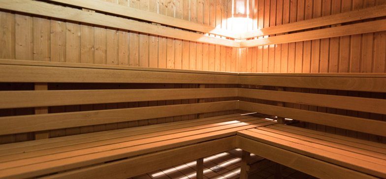 Wnętrze sauny fińskiej obite jasnym drewnem. Wzdłuż ścian drewniane ławy z dwoma rzędami siedzisk.