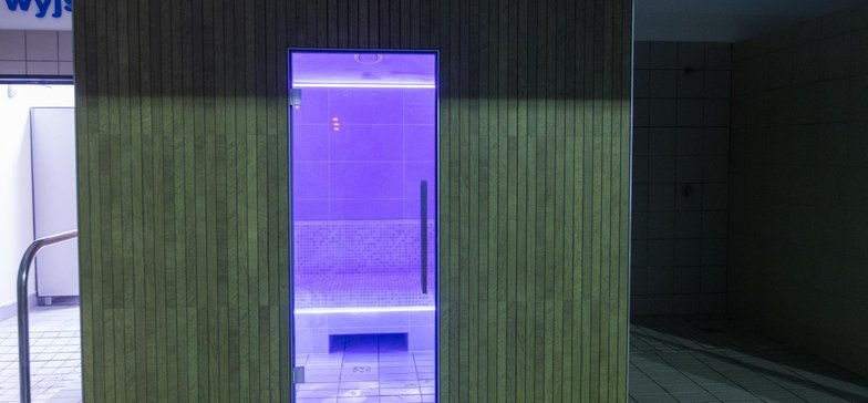 Sauna parowa od zewnątrz obita ceramiką imitującą cienkie, drewniane deski. Wnętrze sauny podświetlone w kolorze fioletowym.