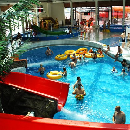 Indoor pool with inside slides: orange and red. There are many people in the water with yellow pontoons. 