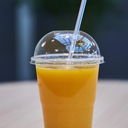 Świeżo wyciskany sok z pomarańczy w plastikowym kubku z pokrywką i słomką. 